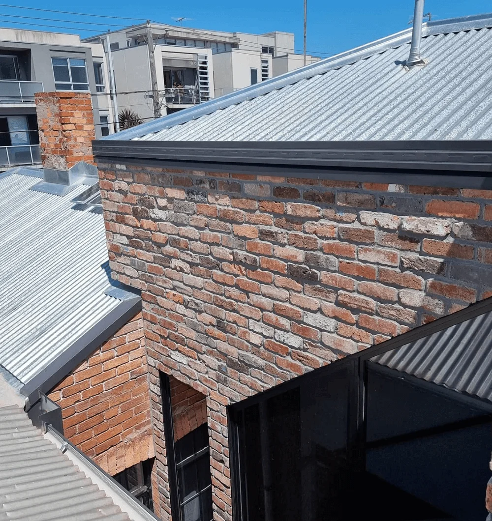 A house with brick walls and metal roofing under a clear sky.