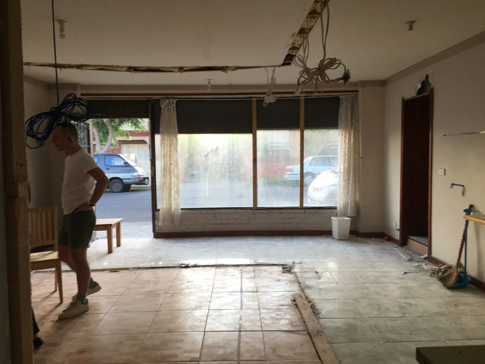 Man standing in an empty, under-renovation room with large front windows.