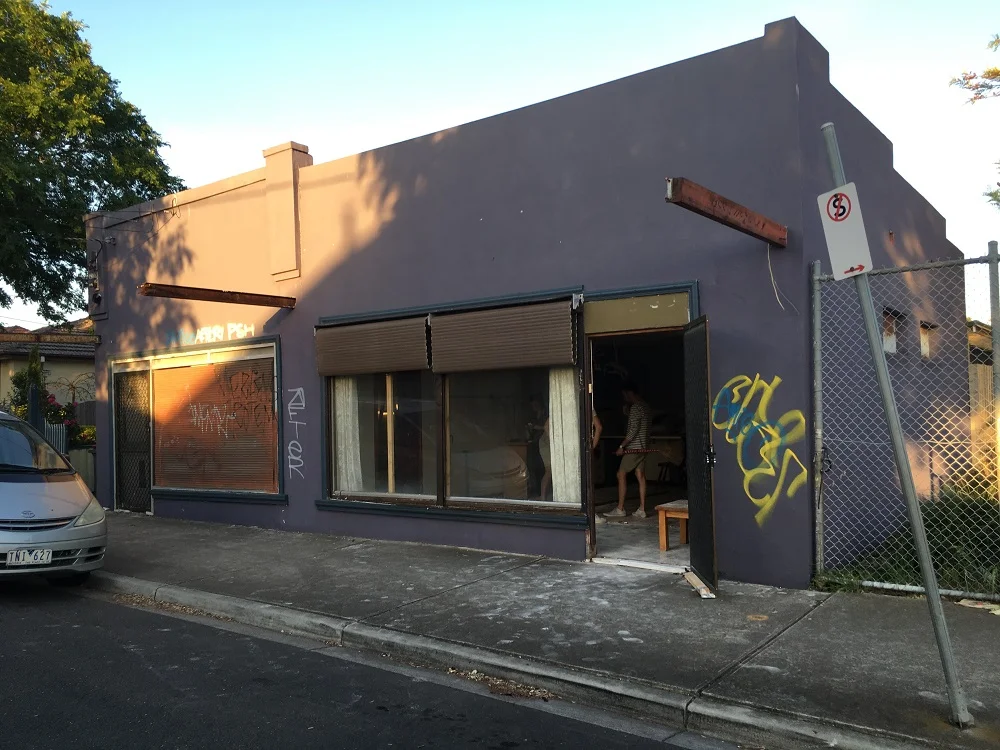 Empty storefront with graffiti on purple walls at sunset.