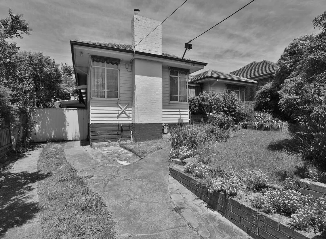 Black and white image of a suburban house with a garden.