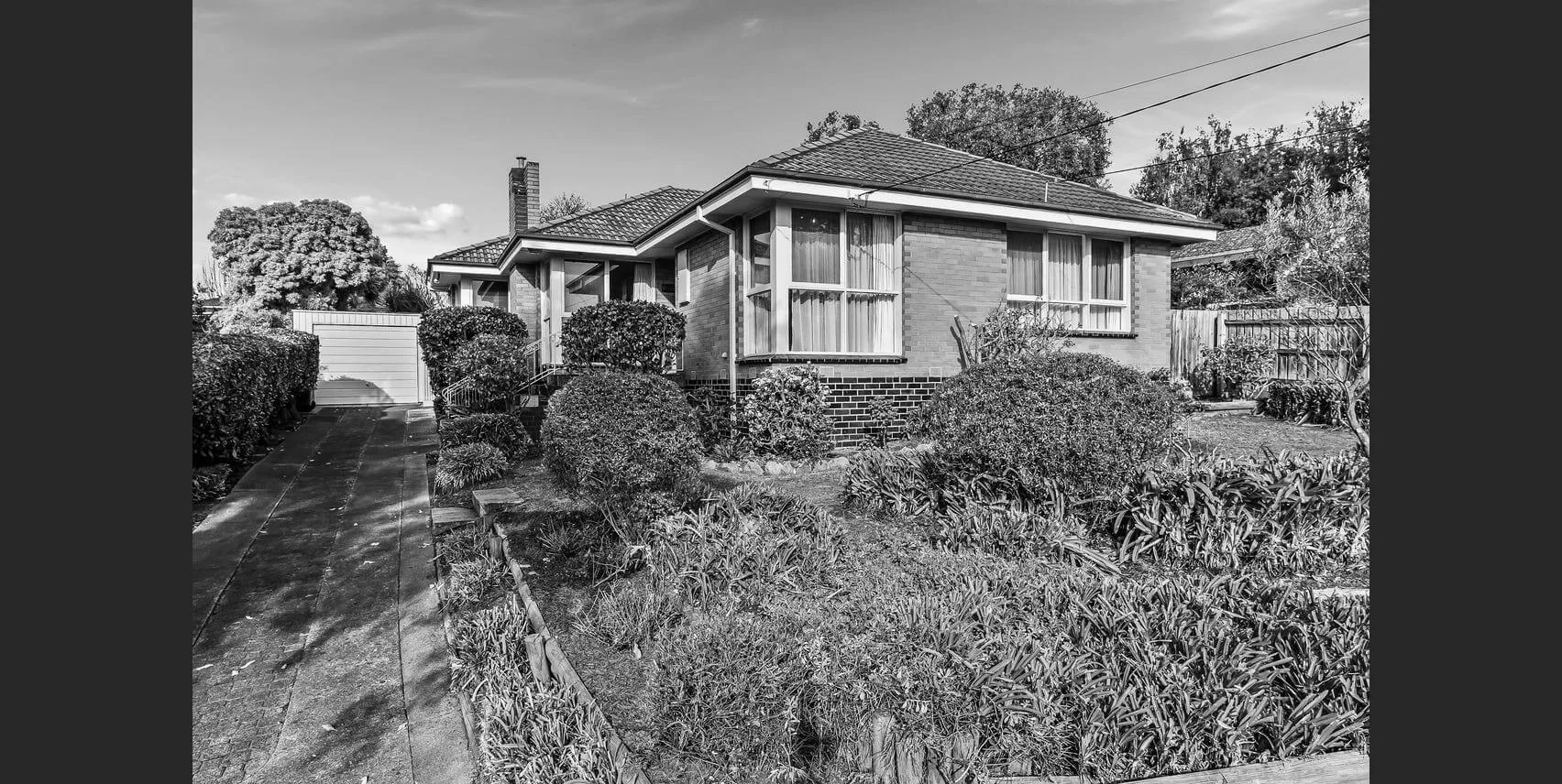 Black and white image of a suburban house with a garden.