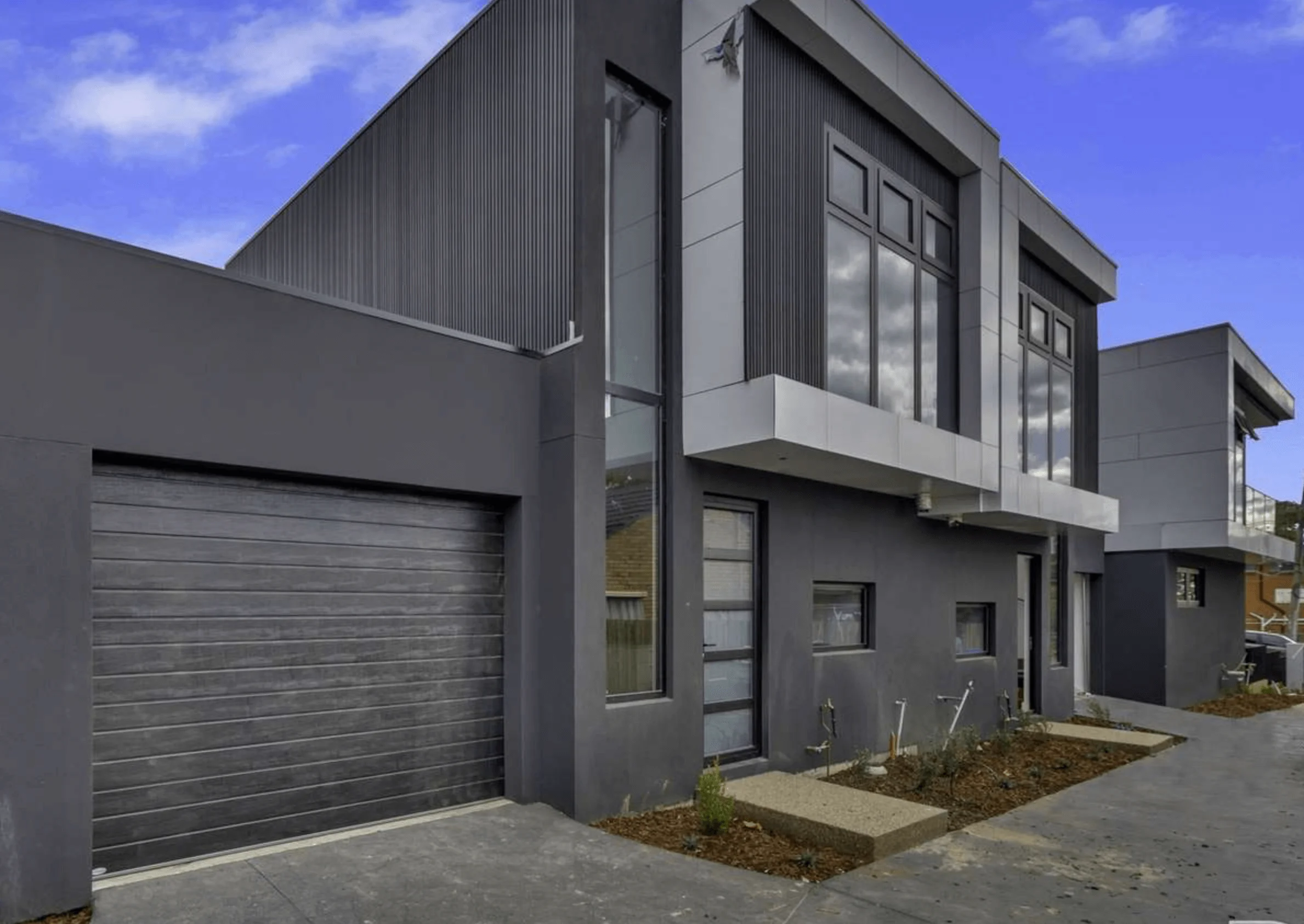 Modern dark gray two-story house with large windows and garage.